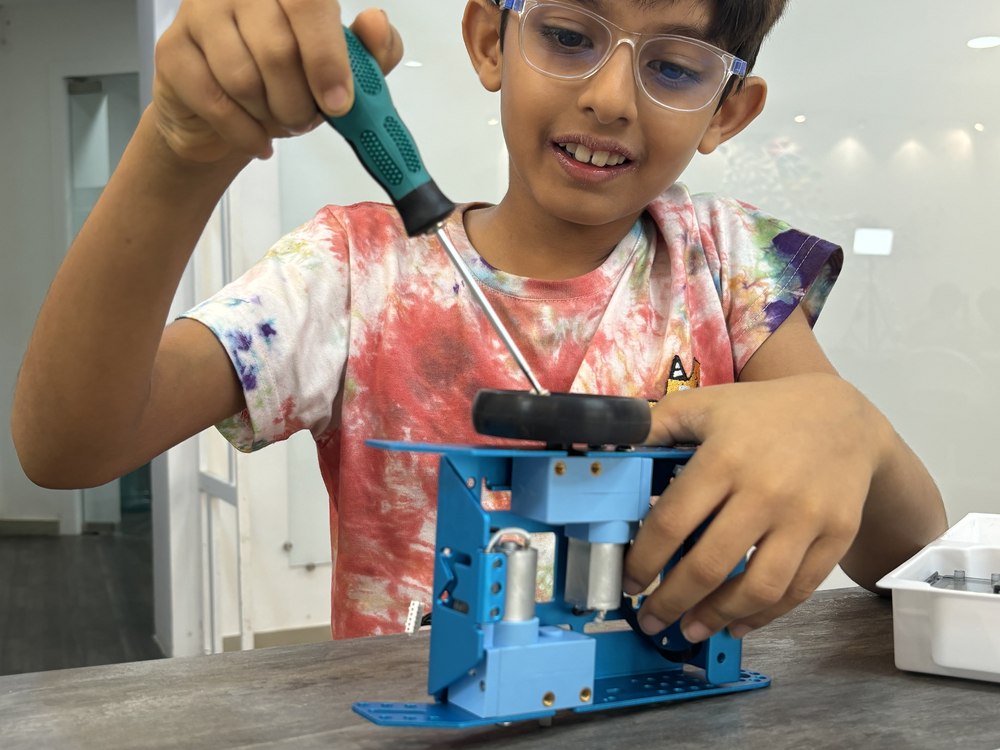 A Cubo Academy child smiling as he assembles his robot with a screwdriver